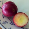 un fruit de prunus globus coupé en deux sur une assiette, un côté chair jaune clair, un côté peau rouge