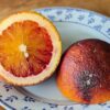 orange sanguine violette de la vallée, coupée en deux, une face chair, une face peau, posée sur une assiette blanche à petites fleurs bleues