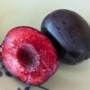 Un fruit d'aprisali coupé en deux, 1 côté chair rouge, 1 côté peau bleu